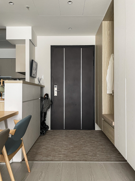 空間整體以白色與暖色木紋為主,在玄關與廚房間相隔的中島吧檯,將對外櫃體規劃為小孩的使用空間,未來可放置書包、餐袋等等,收納櫃門片把手高度也設計符合學齡兒童使用的尺寸。玄關櫃的設計附有吊衣桿與穿衣鏡,讓進出的家人都可整理自己的衣著,也不必將灰塵帶入房間內