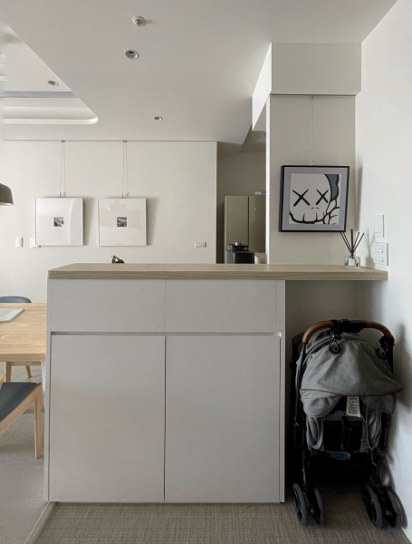 空間整體以白色與暖色木紋為主,在玄關與廚房間相隔的中島吧檯,將對外櫃體規劃為小孩的使用空間,未來可放置書包、餐袋等等,收納櫃門片把手高度也設計符合學齡兒童使用的尺寸